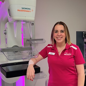 Mammographer in pink shirt standing next to x-ray machine