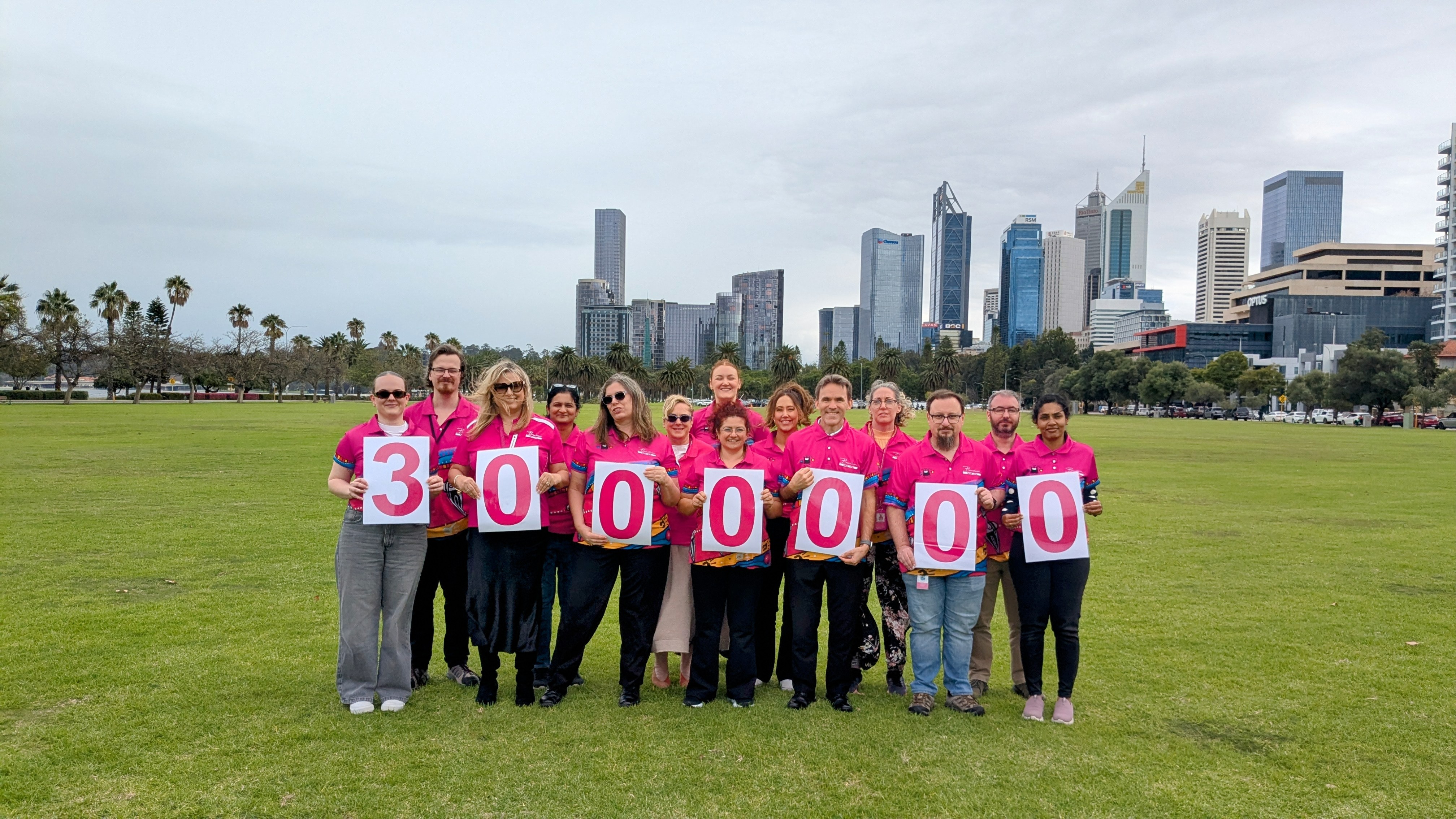 A group of people in pink shirts stand together with signs reading 3 Million